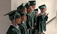  A group of young children wearing green caps and gowns look on.